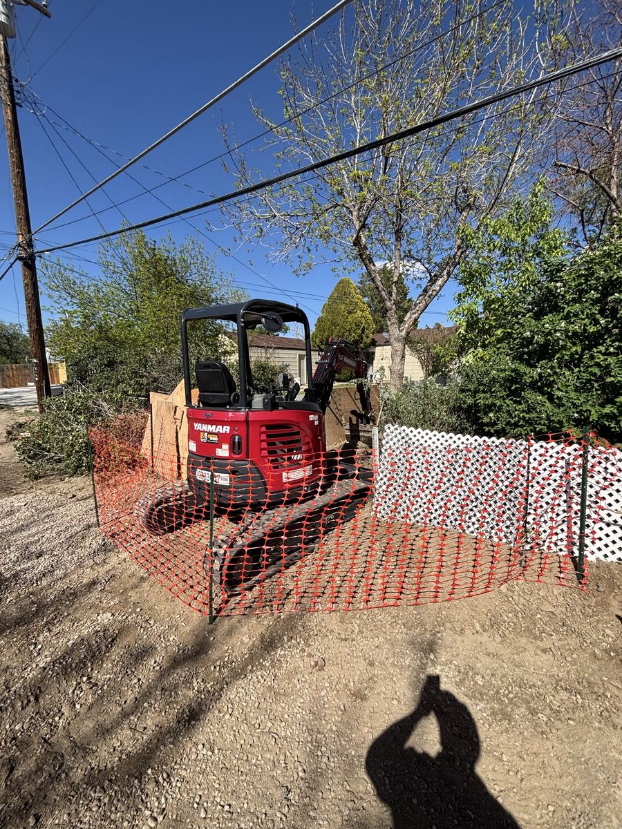 Mini excavator with orange safety fencing set up for a sewer line excavation at a Pueblo, Colorado home